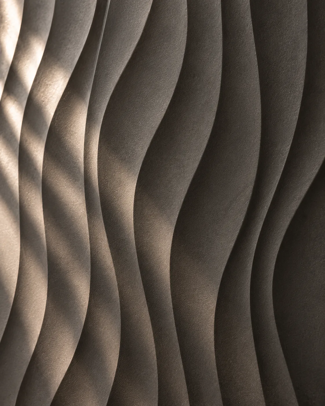 Sculpted charcoal wall surface with broad flowing wave relief and gentle shadow gradients